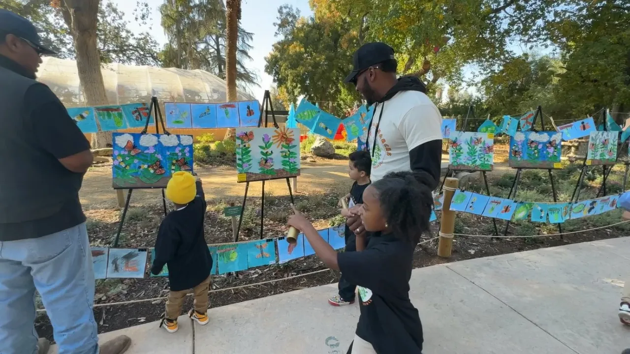 Black children looking at paintings in a field with two adults.