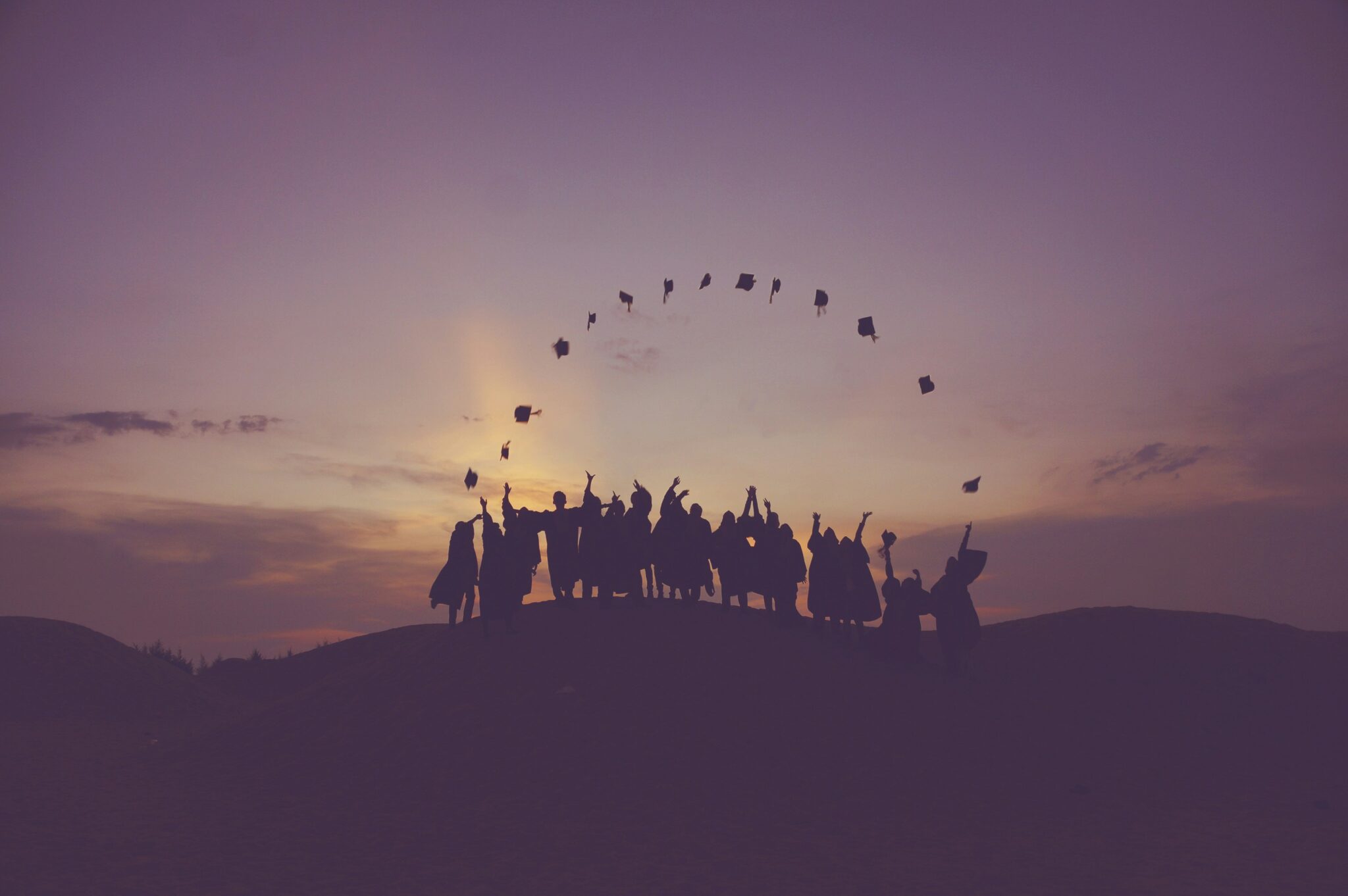 photo of gradutes throwing their hats in the air with a sunset backdrop